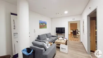 Geräumiger Wartebereich mit bequemen Sofas, einem Fernseher und einem Durchgang zu einem weiteren Raum.
