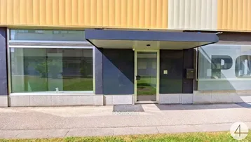 Moderne Gebäudefassade mit großen Fenstern und einem überdachten Eingangsbereich, der zum Gebäude führt.