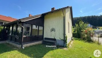 Seitenansicht des Hauses mit einem Wintergarten und einem gepflegten Rasenbereich unter blauem Himmel.