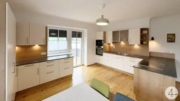 Moderne Küche mit hellen Schränken, Holzakzenten, Kochinsel und Blick ins Grüne durch das Fenster.