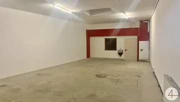 Großer, leerer Raum mit Betonboden, weißen Wänden und rotem Akzentbereich, inklusive Fenster und Tür.