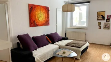 Helles Wohnzimmer mit Sofa, Couchtisch, farbenfrohem Kunstwerk und Fenster für natürliches Licht.