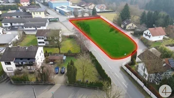 Luftaufnahme eines grünen Baugrundstücks in ländlicher Umgebung mit umliegenden Wohnhäusern und Straßenanbindung.