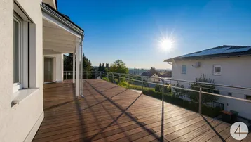 Große Holzterrasse mit Edelstahlgeländer und weitem Blick über die Landschaft unter strahlend blauem Himmel.
