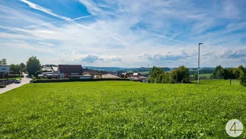 Weitläufige Grünfläche mit Blick auf die umliegende Landschaft und Wohnbebauung unter blauem Himmel.