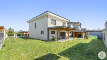 Modernes Einfamilienhaus mit großem Garten, überdachter Terrasse und Spielbereich für Kinder.