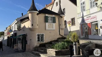 Historisches Gebäude mit Türmchen und Kopfsteinpflaster in einer malerischen Altstadtgasse unter blauem Himmel.