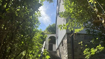 Alter Steinweg führt zu einem charmanten Haus, umgeben von üppigem Grün unter blauem Himmel.