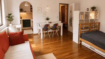 Helles, offenes Wohn-Esszimmer mit Holzboden, Schlafbereich und integrierter Küche.