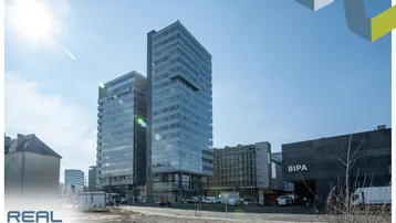 Moderne Hochhäuser mit Glasfassaden und sonnigem Himmel, umgeben von städtischer Infrastruktur.