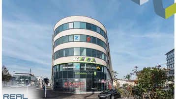 Modernes, geschwungenes Geschäftsgebäude an einer Straßenecke mit großen Fenstern und klarem Himmel.