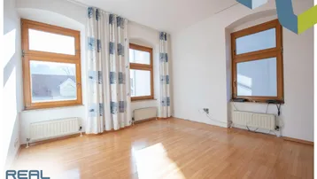 Helles Zimmer mit Parkettboden, mehreren Fenstern und Heizkörpern, bereit zur individuellen Gestaltung.