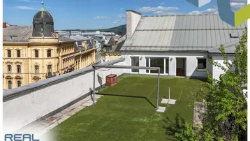 Dachterrasse mit Kunstrasen und Blick auf die umliegende Stadtarchitektur unter blauem Himmel.