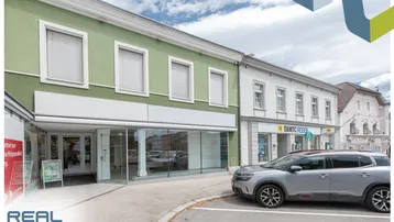 Ansicht der Geschäftsfassade mit großen Schaufenstern und einem geparkten Auto davor.