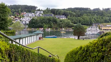 Panoramablick auf den See mit umliegenden Häusern und grüner Landschaft unter bewölktem Himmel.