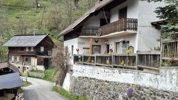 Traditionelles Haus in ländlicher Umgebung mit Holzbalkon, Steinfassade und Blick auf grüne Hügel.
