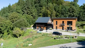 Zwei moderne Häuser mit Holzfassade und Blick auf den bewaldeten Hügel.