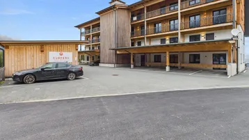 Modernes Holzgebäude mit mehreren Balkonen und Außenparkplätzen in alpiner Umgebung.