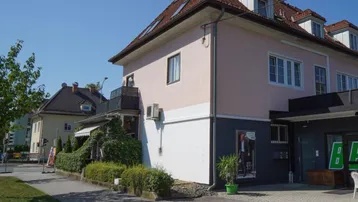 Ansicht des Gebäudes mit rosa Fassade, roten Dachziegeln und einem kleinen Balkon an der Seite.