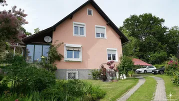 Rosa verputztes Einfamilienhaus mit Satteldach, Vorgarten und gepflasterter Auffahrt.