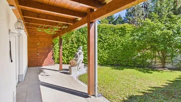 Überdachte Terrasse mit Holzbalken und Blick auf den gepflegten Gartenbereich.
