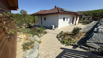 Modernes Einfamilienhaus mit gepflastertem Weg, Steingarten und Photovoltaikanlage auf dem Dach.
