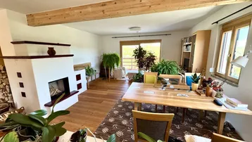Helles Wohnzimmer mit Holzbalken, Kamin und Zugang zu einem Außenbereich mit viel Grün.