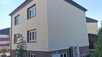 Modernes Gebäude mit heller Fassadenverkleidung und sichtbarer Wärmepumpe im Außenbereich.