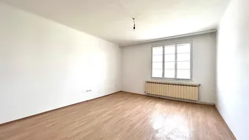 Heller, leerer Raum mit weiß gestrichenen Wänden, Laminatboden und einem Fenster mit Heizkörper darunter.