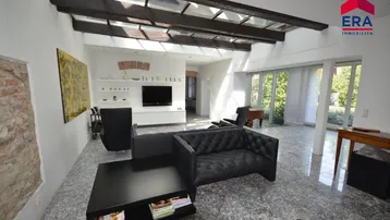 Helles Wohnzimmer mit Glasdach, dunklen Holzbalken und modernem Mobiliar auf Steinboden.