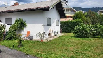 Gepflegter Gartenbereich neben einem Einfamilienhaus mit weißer Fassade und Satteldach.