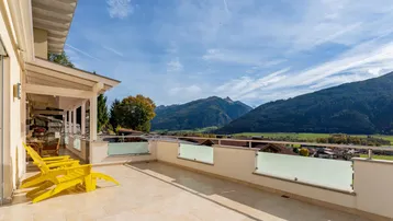 Große Sonnenterrasse mit gelben Stühlen und beeindruckendem Bergblick unter blauem Himmel.