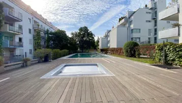 Große Holzterrasse mit Gemeinschaftspool und Whirlpool, umgeben von modernen Wohngebäuden.