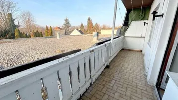 Heller Balkon mit weißem Holzgeländer und weitem Blick über die Dächer und Bäume.