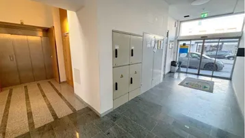 Heller Eingangsbereich eines Gebäudes mit Aufzug, elektrischen Schalttafeln und Zugang zur Straße.