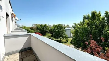 Geräumiger Balkon mit Fliesenboden und weitem Blick ins Grüne unter blauem Himmel.