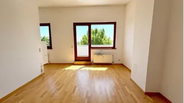 Helles, leeres Zimmer mit Parkettboden und Zugang zu einem Balkon, ideal für Wohnzwecke.