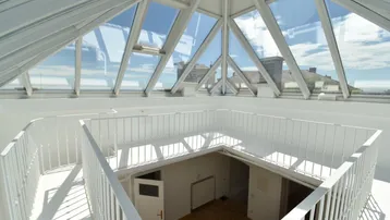 Heller Innenraum mit großer Glasdachkonstruktion und Blick auf die Umgebung, der viel Tageslicht hereinlässt.