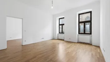 Helles, leeres Zimmer mit Parkettboden und hohen Fenstern, bereit zur individuellen Gestaltung.