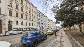 Blick auf eine belebte Stadtstraße mit parkenden Autos und historischen Gebäuden.