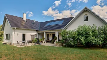 Rückansicht eines modernen Hauses mit großer Rasenfläche, Terrasse und Solarpaneelen auf dem Dach.