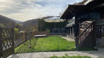 Gepflegter Gartenbereich mit Rasenfläche, Holzhaus und Sitzgelegenheit unter einem Sonnenschirm.