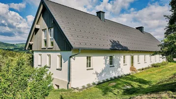 Ländliches Haus mit Satteldach und weißer Fassade, umgeben von grüner Hügellandschaft.