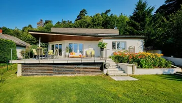 Modernes Haus mit großer Sonnenterrasse, Gartenmöbeln und blühenden Blumenbeeten.