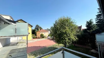 Heller Balkon mit Glasgeländer und Blick auf die umliegende Wohngegend und Bäume.