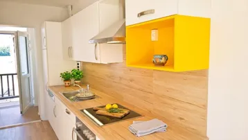 Moderne Küche mit weißen Schränken, Holztheke, Induktionskochfeld und gelbem Akzentregal.