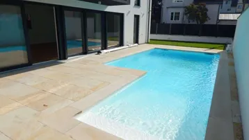 Langer, rechteckiger Pool mit hellem Fliesenrand und Zugang zu den Innenräumen des Hauses.