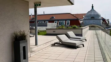 Helle Dachterrasse mit Liegestühlen und Blick auf historische Dächer und die Stadt.