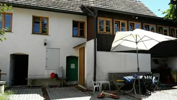 Gemütlicher Außenbereich mit Sitzgelegenheiten und Sonnenschirm vor einem traditionellen Gebäude.