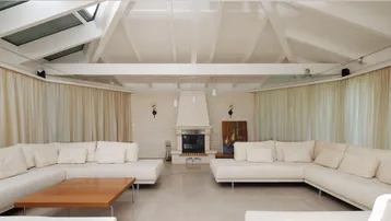 Geräumiges Wohnzimmer mit hohen Decken, Kamin und bequemen weißen Sofas.